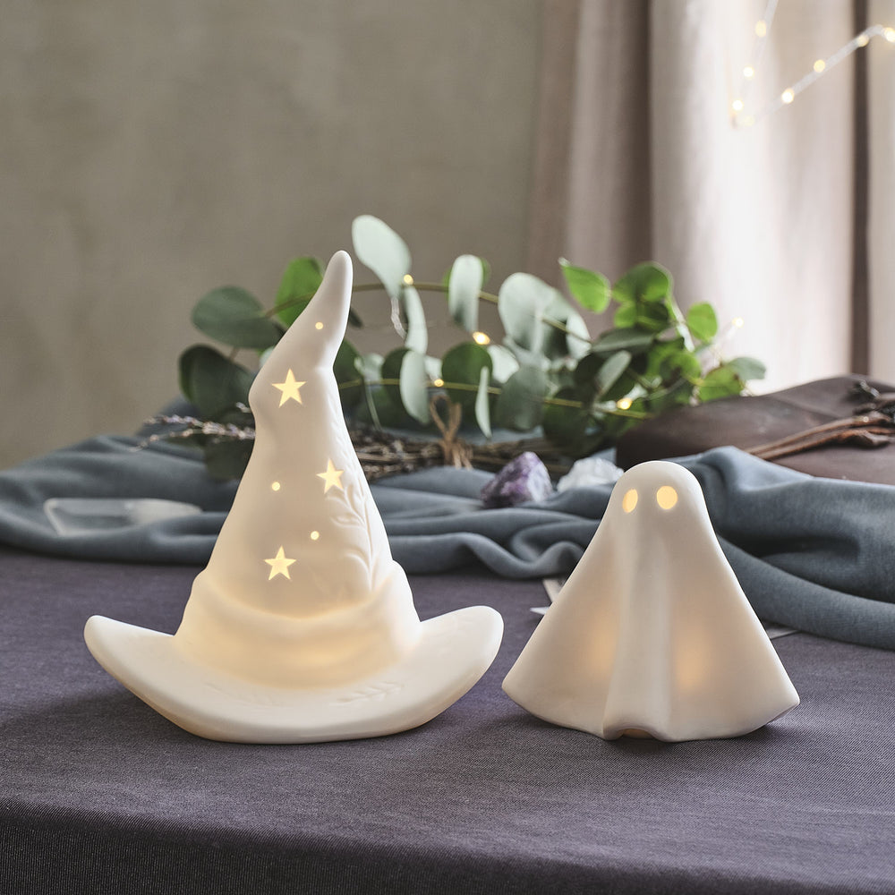 Un chapeau de sorcière en céramique et un fantome en céramique posés sur une table en tant que déco de table d'halloween