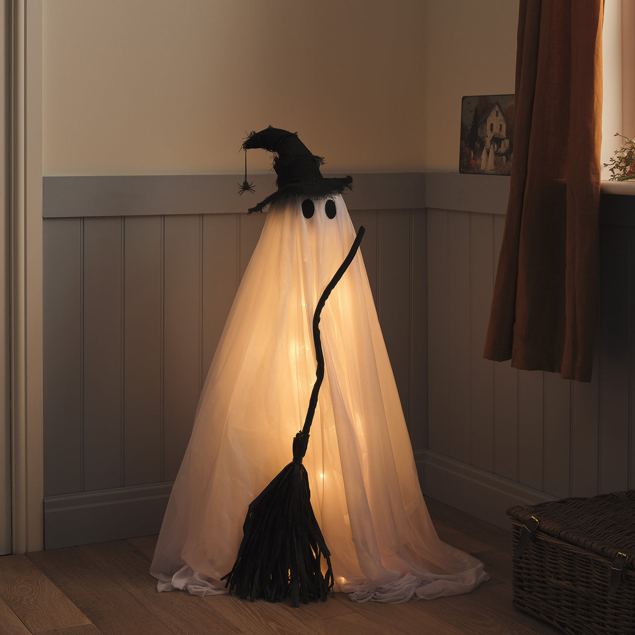 Un fantome avec chapeau et balai de sorcière installé près de la porte d'entrée en déco d'halloween