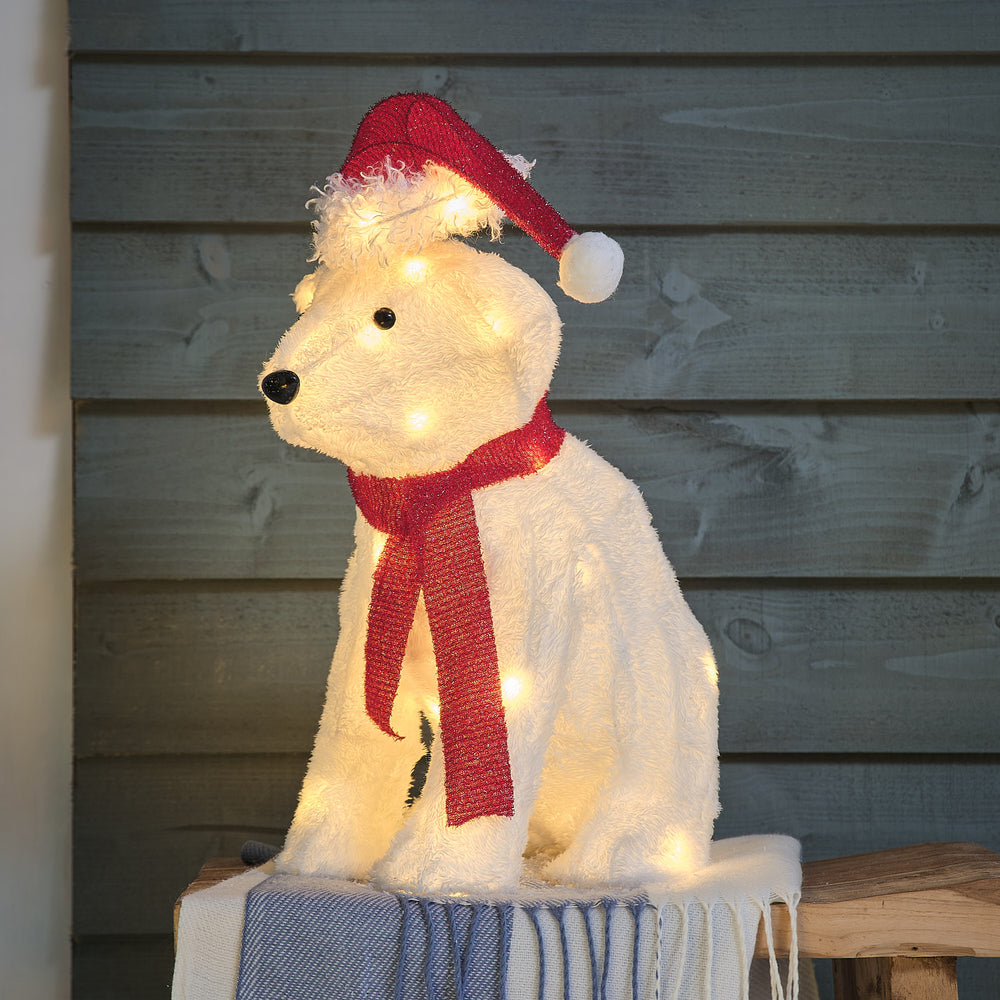 Une figurine illuminée d'un ours blanc portant un bonnet rouge et une écharpe rouge.