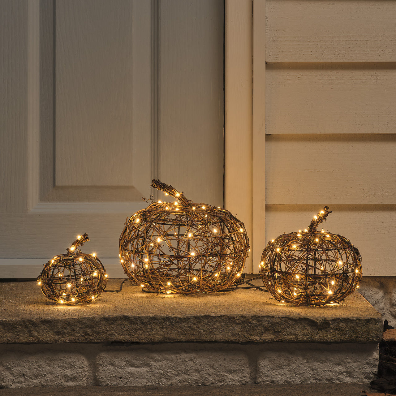 Un lot de 3 citrouilles lumineuses en rotin, posées sur le pas de la porte. une déco d'automne très représentante de la saison et utilisable aussi pour halloween.